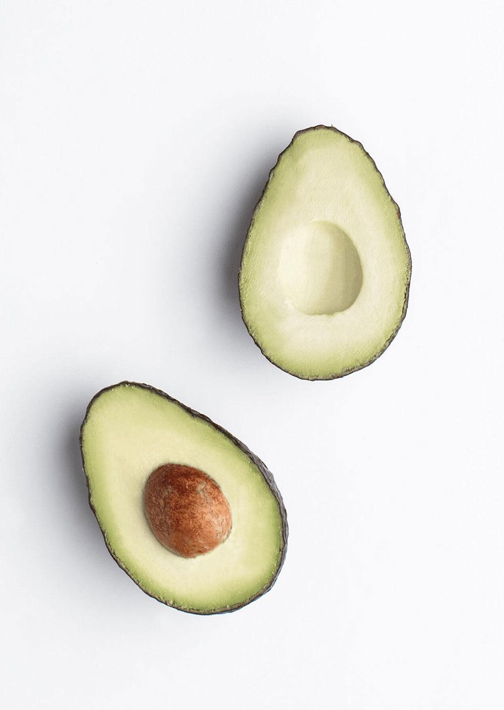 An avocado sliced in half with the pit left in on a white background.
