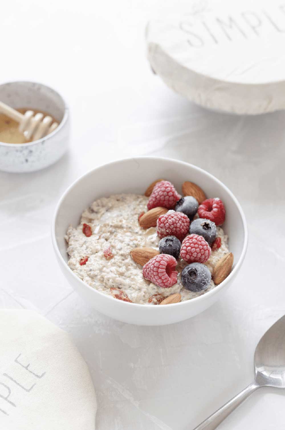 White bowl of oatmeal with berries on top and a small bowl of honey nearby.