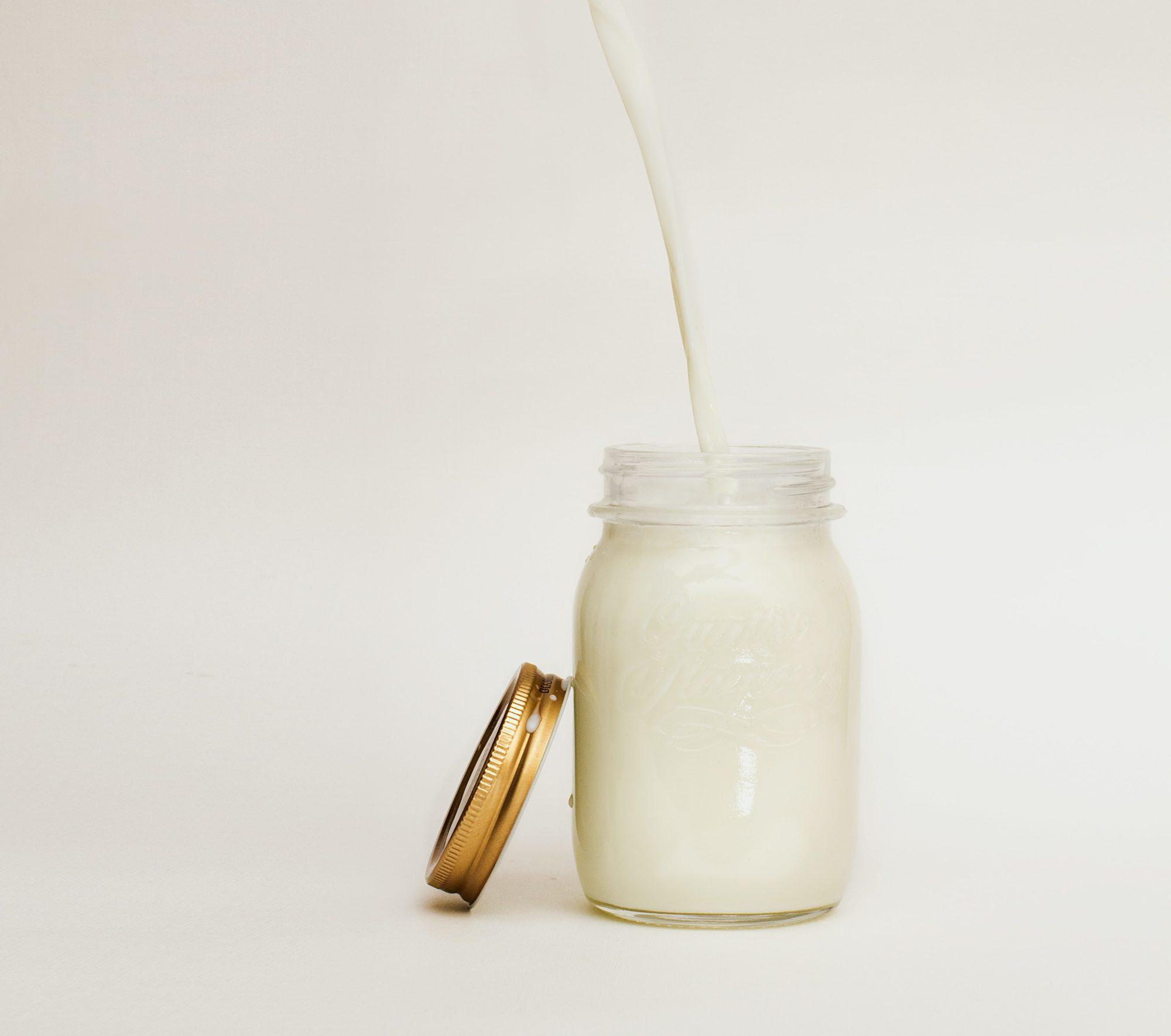Mason jar full of white liquid with a straw in it with a gold lid on a white background.