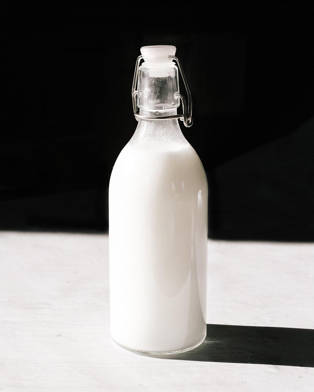 Glass jar of white liquid on a white counter with black background.