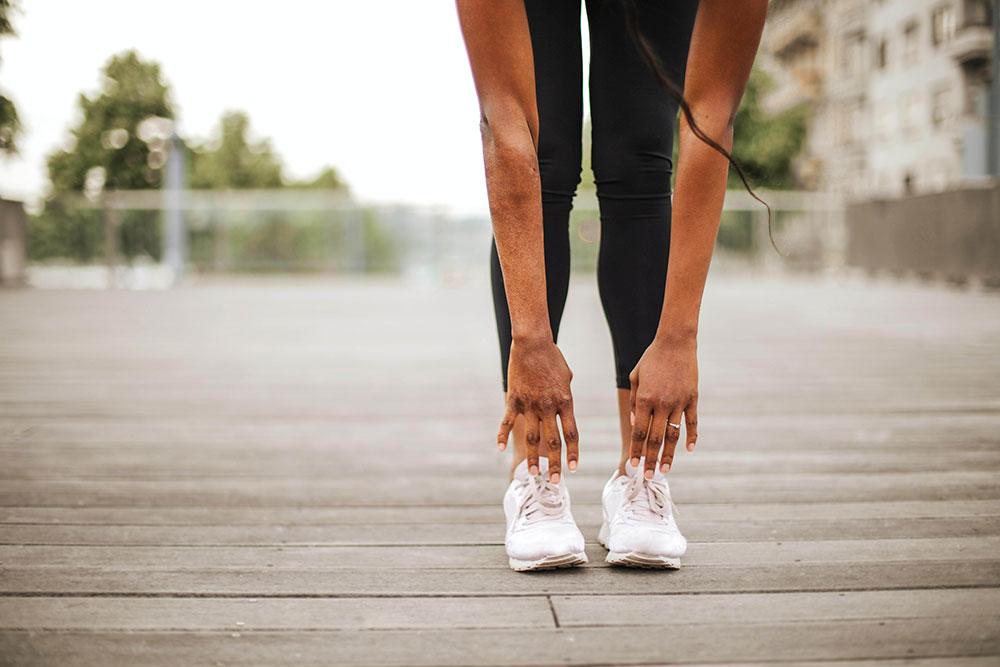 Woman in athletic wear stretching her arms down to her athletic shoes in nature.