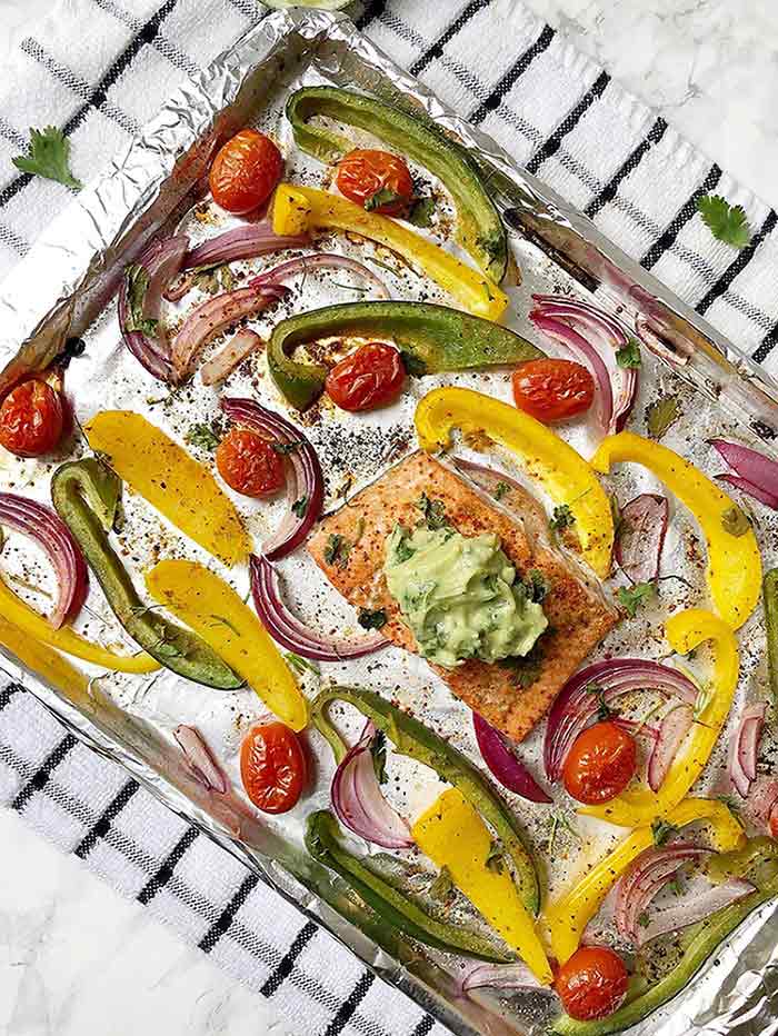 Cooked salmon a cooking tray surrounded by veggies on a black and white striped kitchen towel.