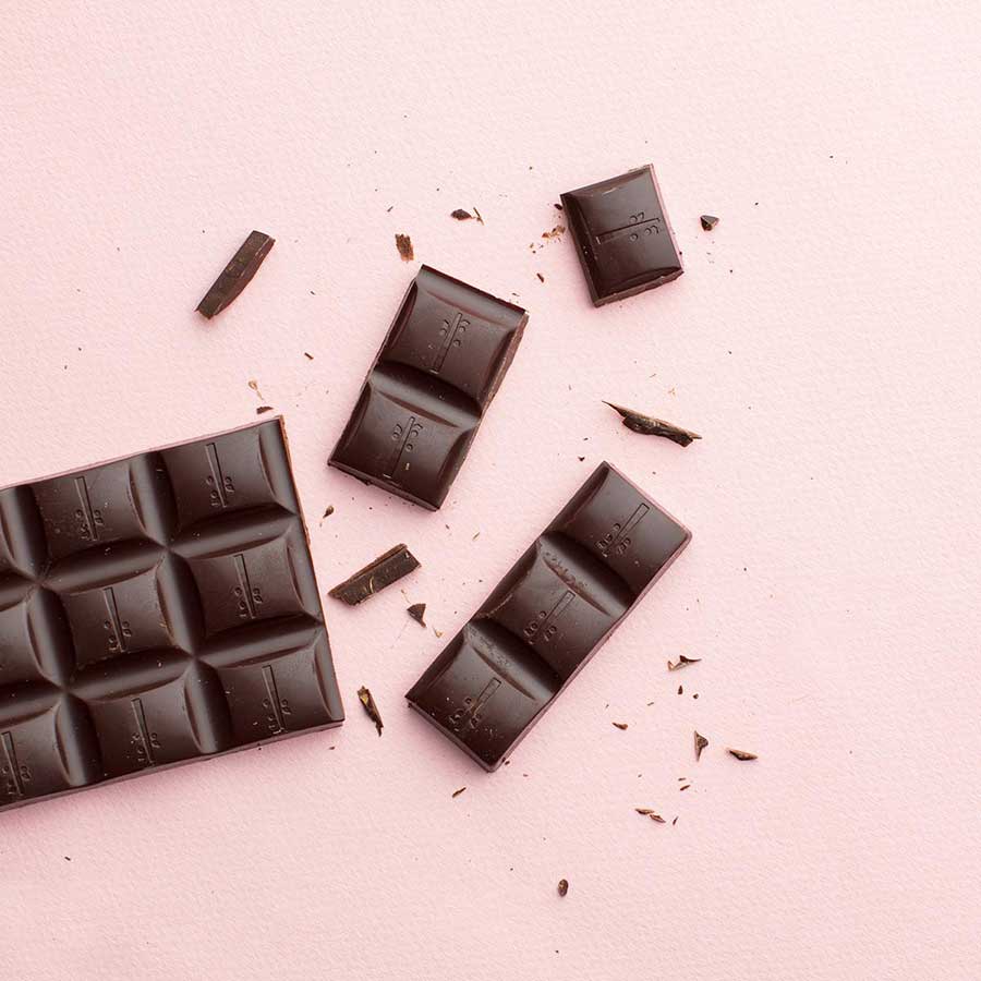 Chocolate bar broken into pieces on a pink background.