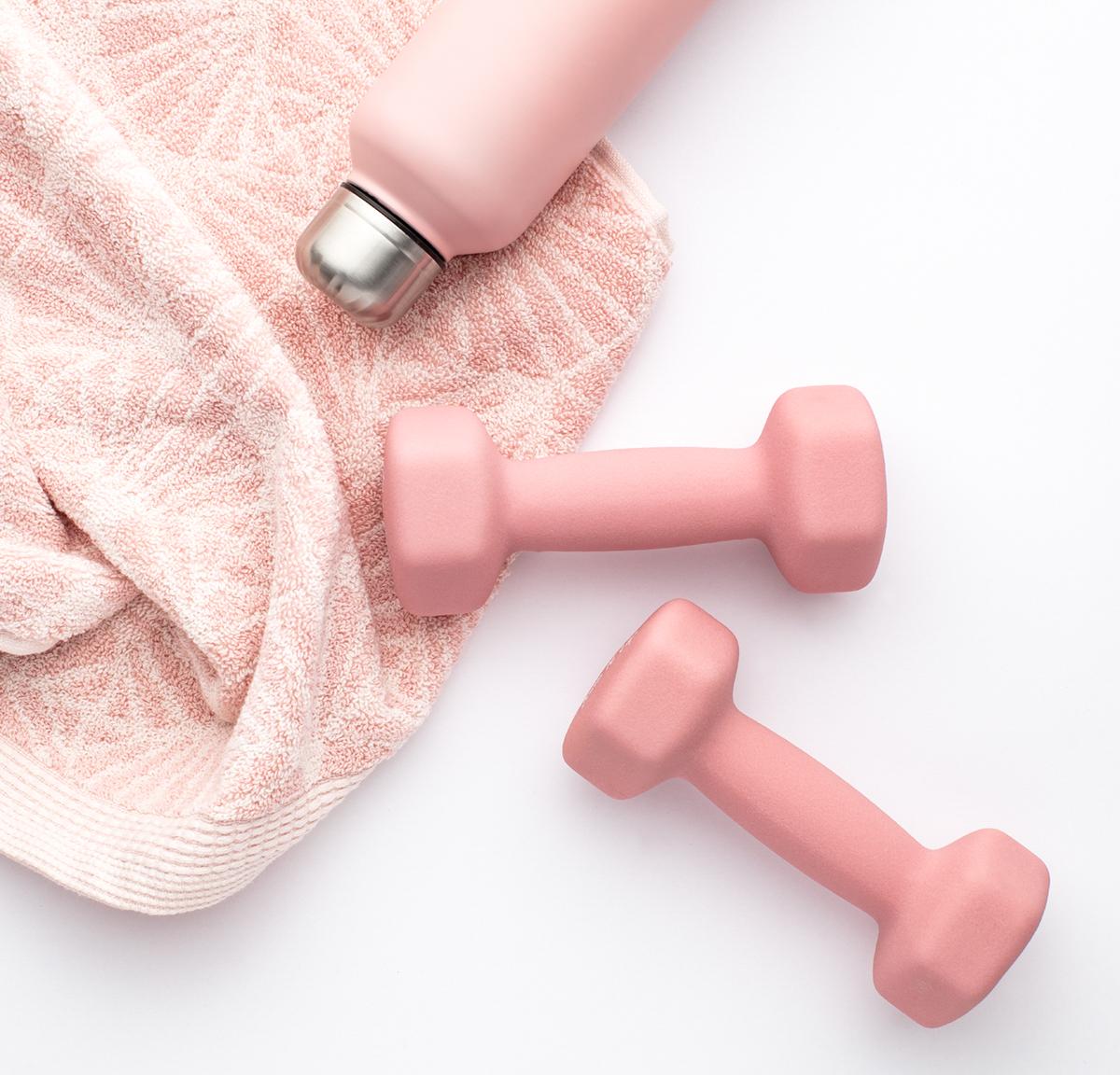 Two small pink weights with a pink towel, with a pink water bottle on a white background.