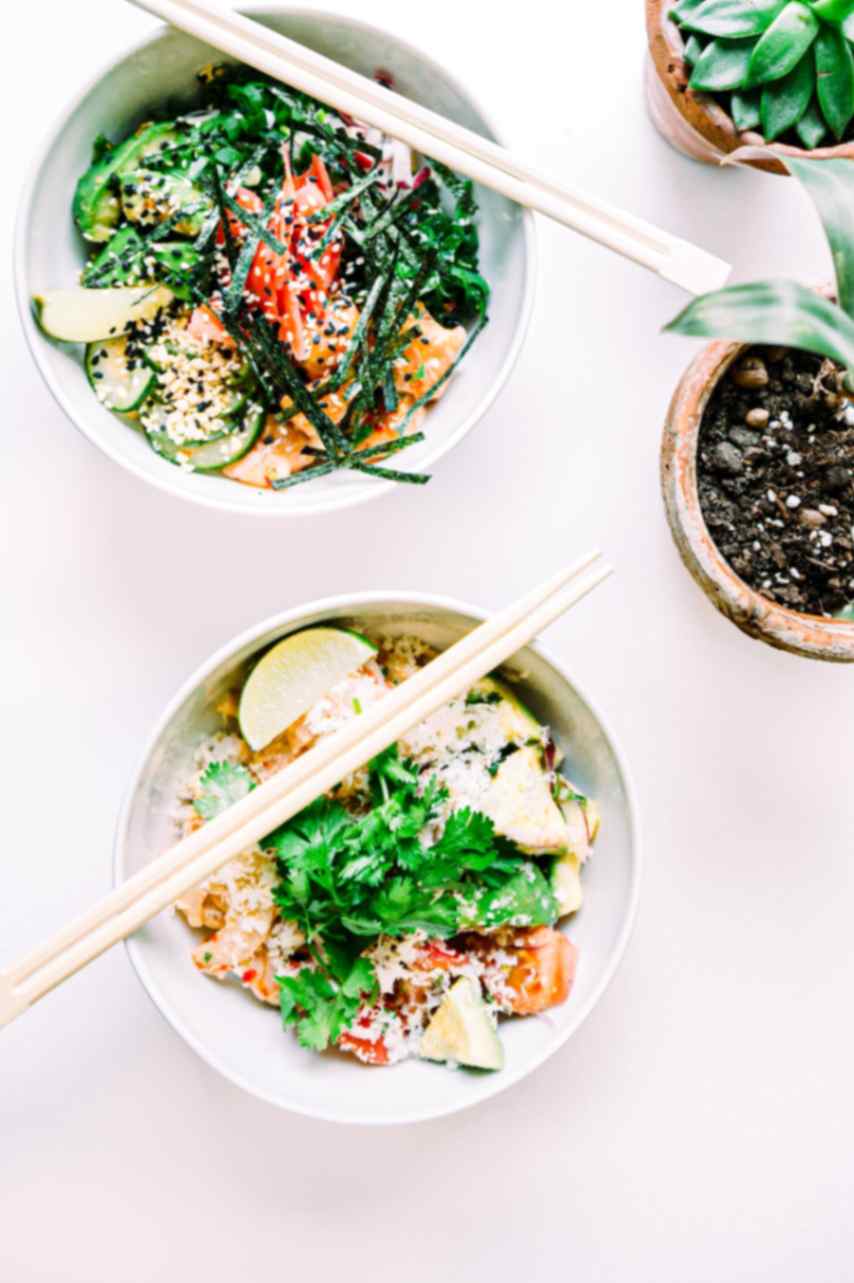 Bowls of food with greens on top and chopsticks.