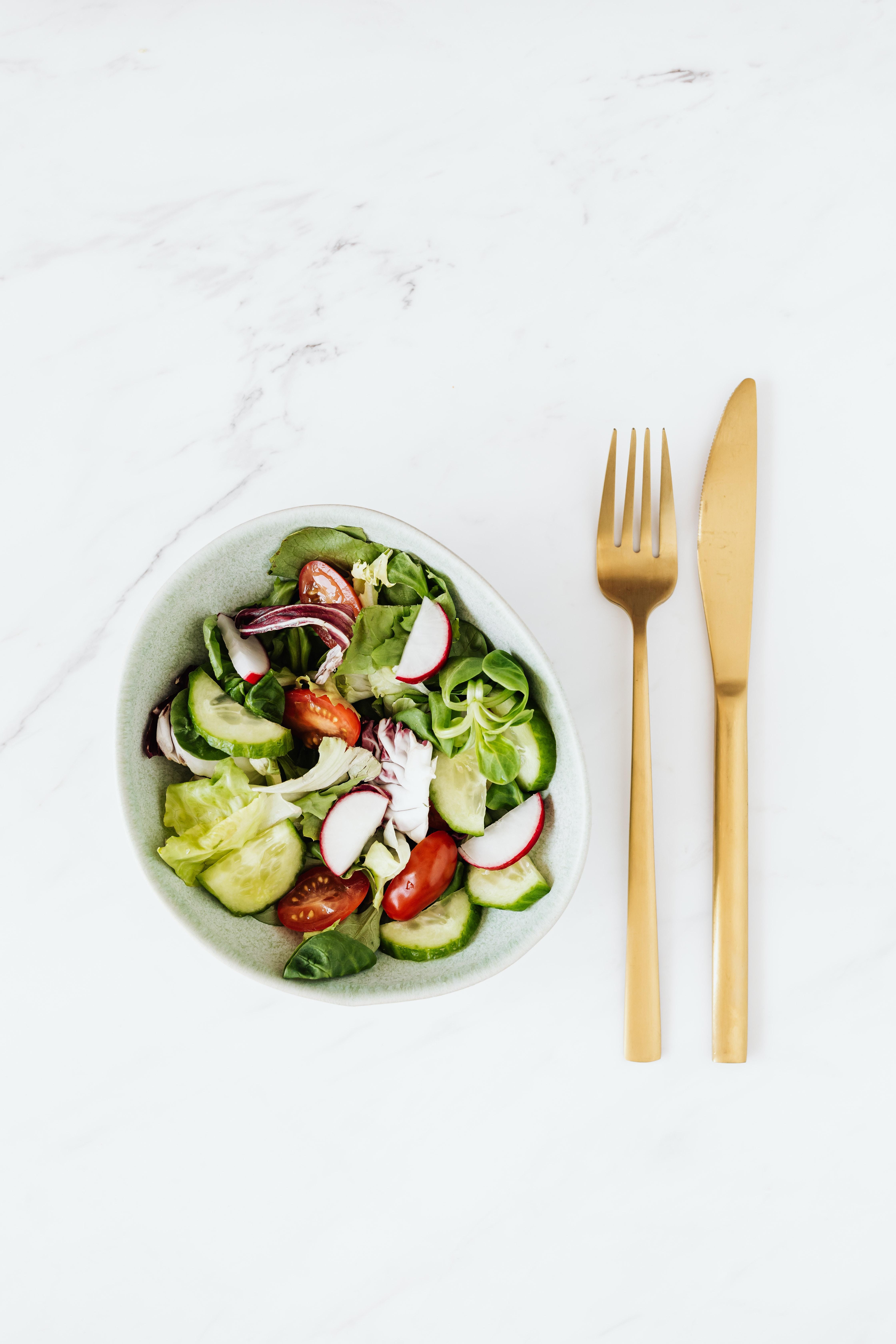 White bowl of a salad on a white background with gold fork and knife next to it.