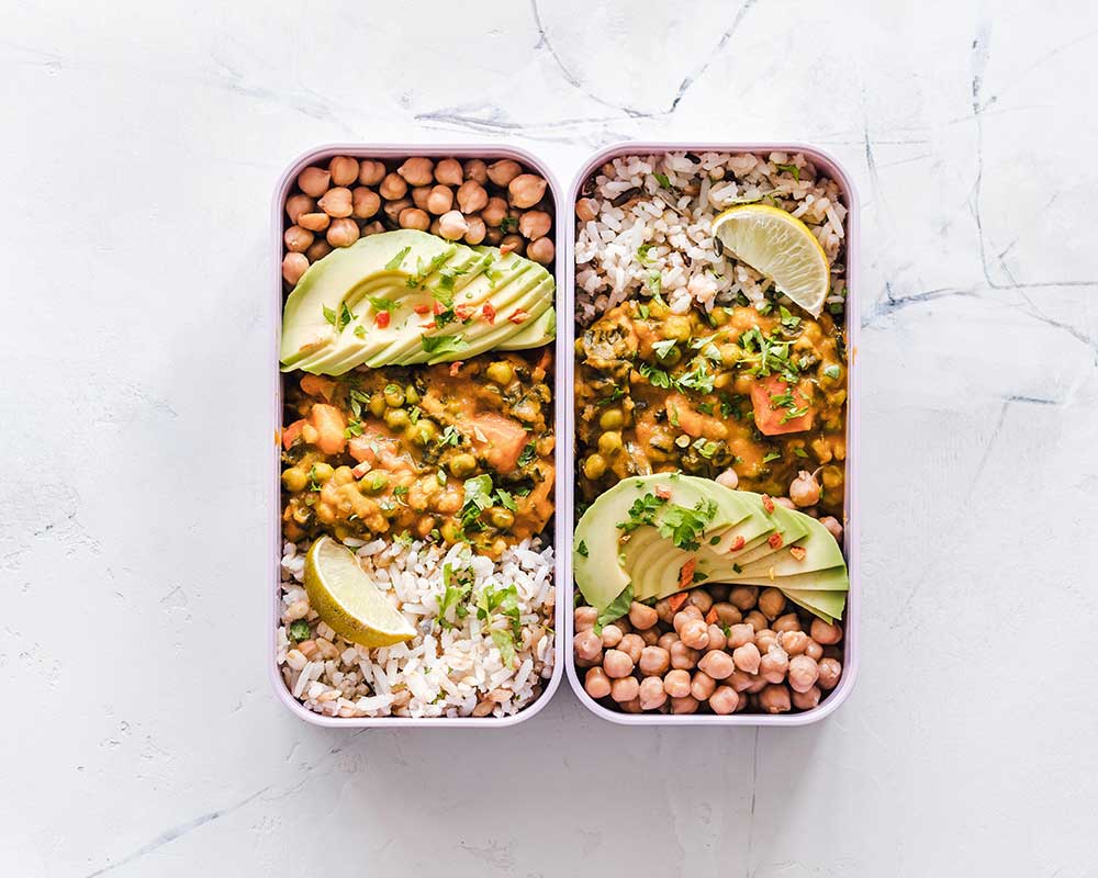 Two containers filled with various food for meal prep on a white white marble counter.