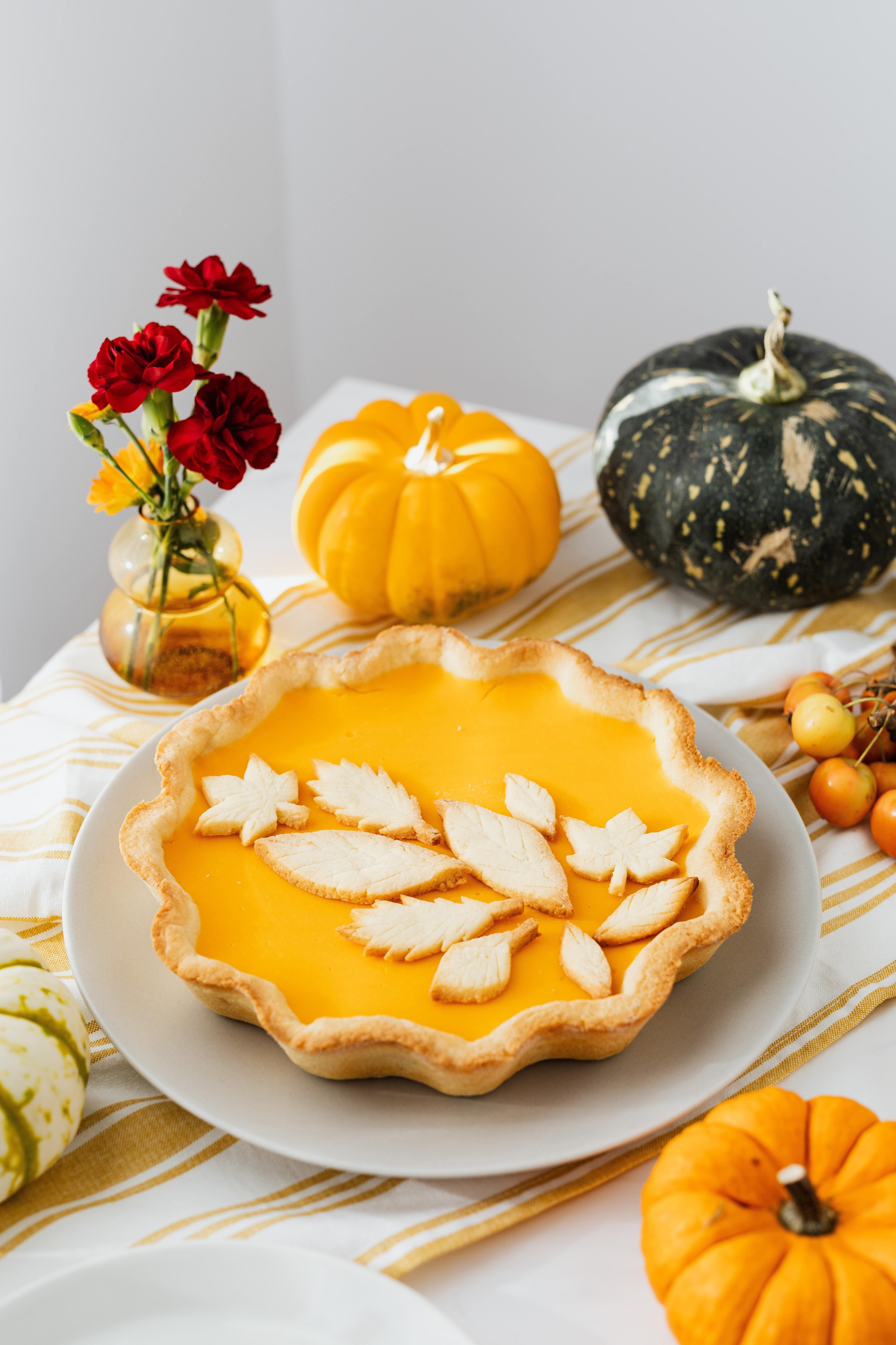 Pumpkin pie on a table with mini pumpkins and a vase of dark red flowers.