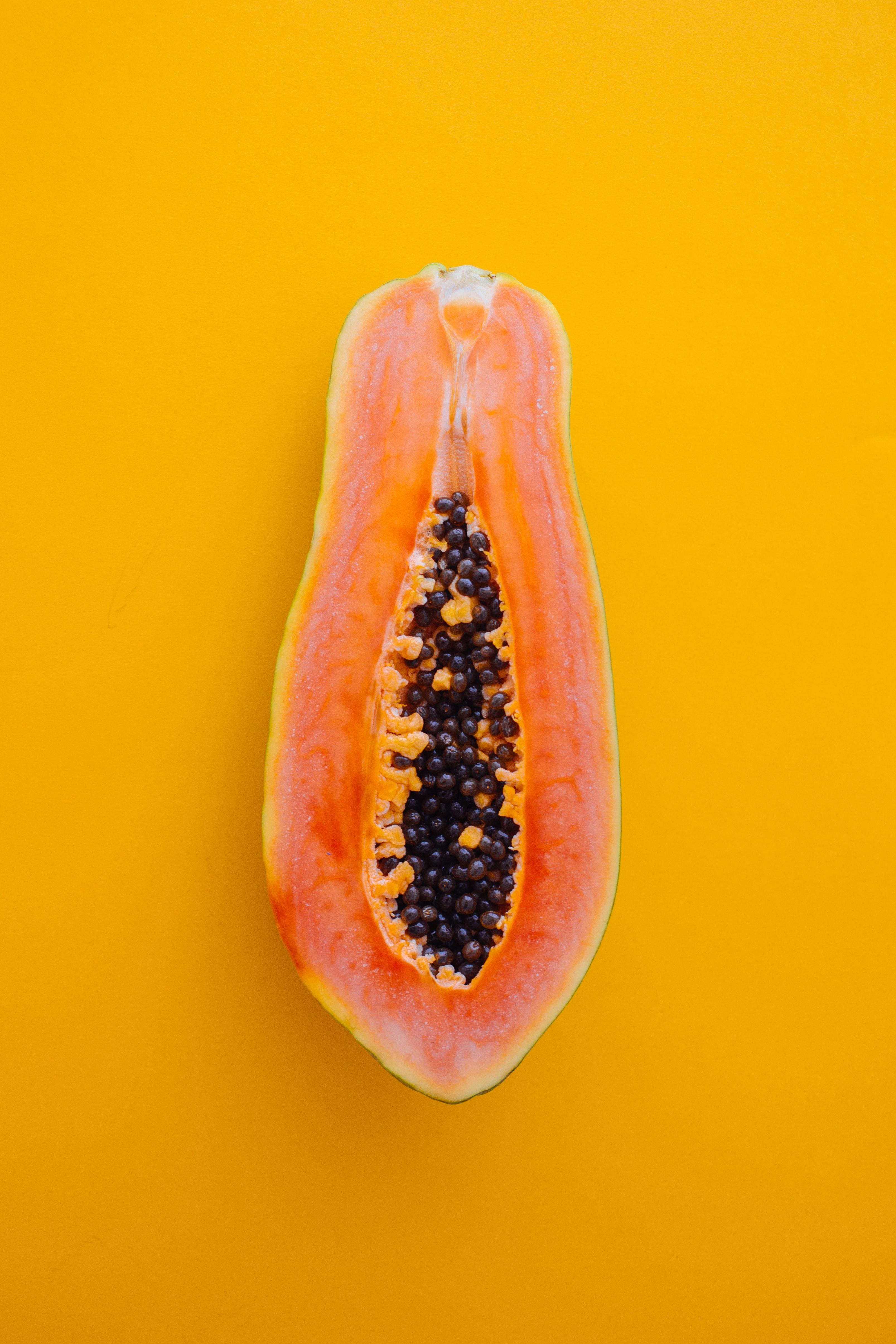 Papaya cut in half exposing black seeds on an orange background.