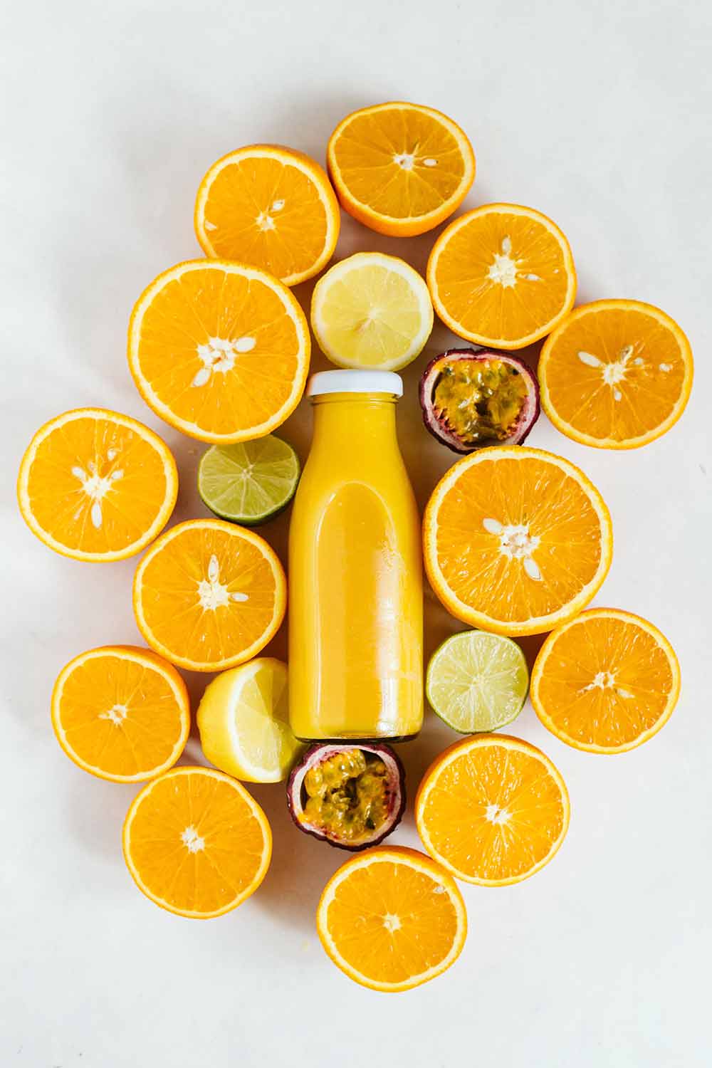 Glass jar full of orange juice surrounded by half cut oranges, lemons and limes on a white background.