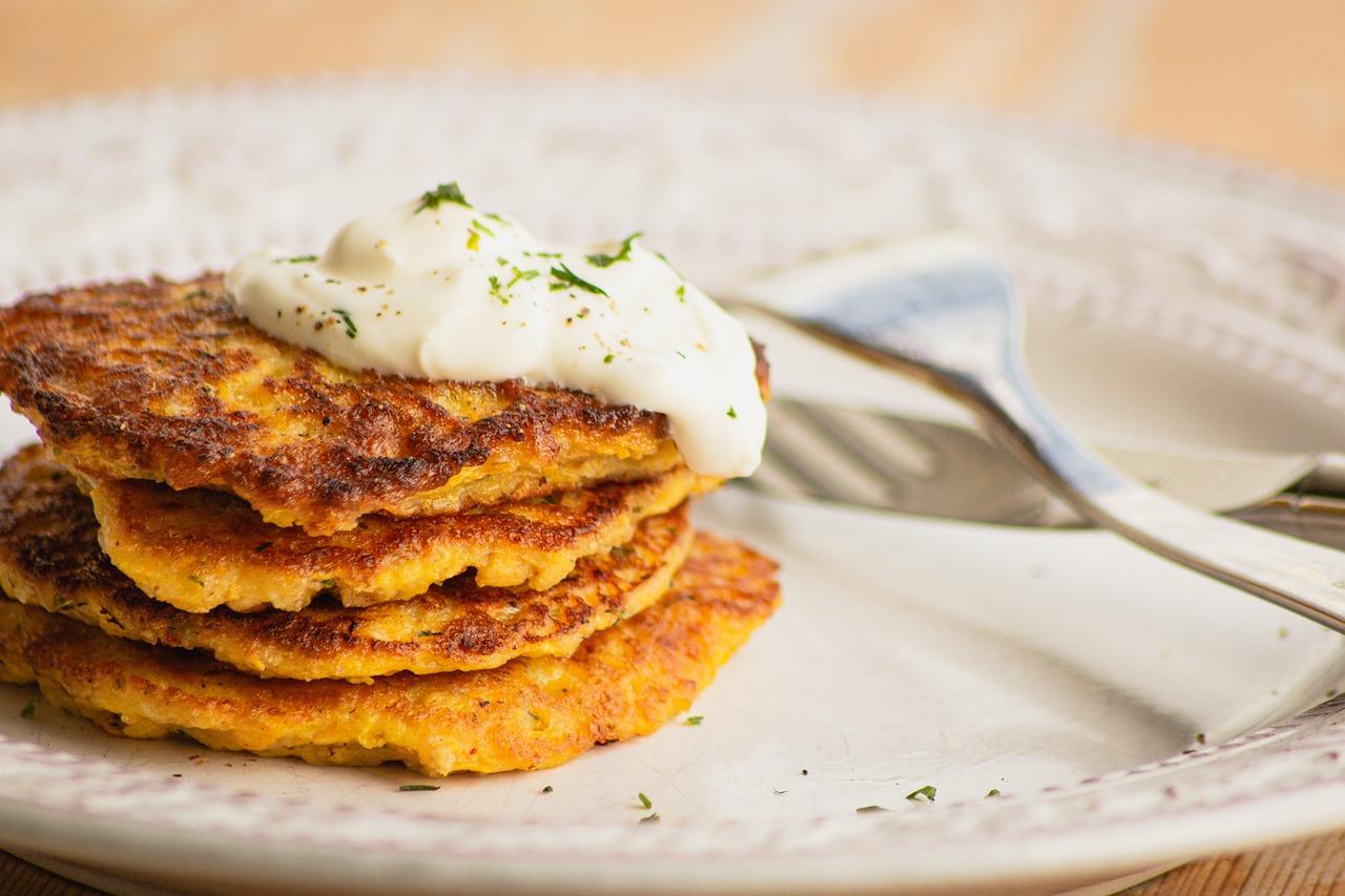 Healthy latke recipe with sour cream and green onion on a white plate with a silver fork laying on top.