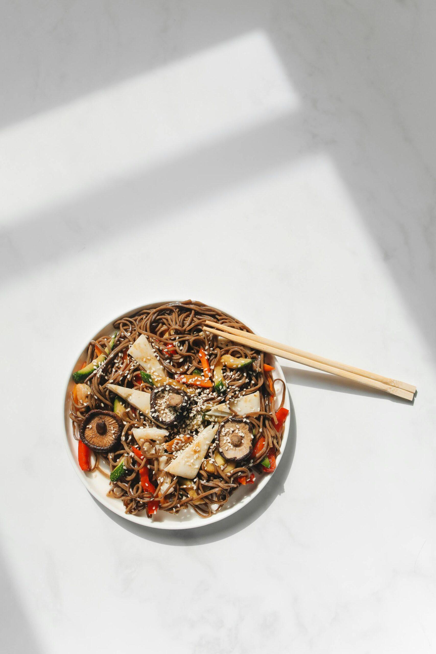 Plate of sesame noodles and veggies with chopsticks on a white countertop
