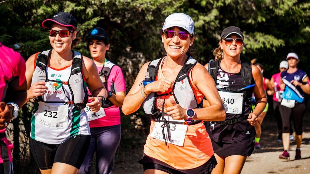 A group of smiling women participating in an outdoor marathon run with race numbers.