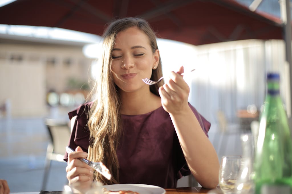 A woman savoring her meal with a smile, dining outdoors in a pleasant setting.