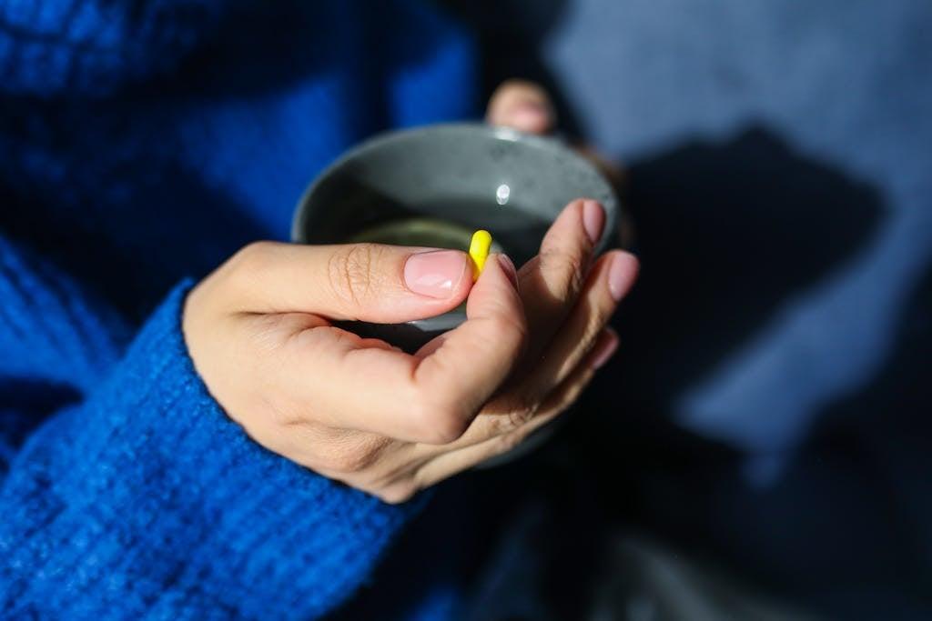 Close-up of hands holding a hot drink and yellow pill, indicating health and wellness theme.