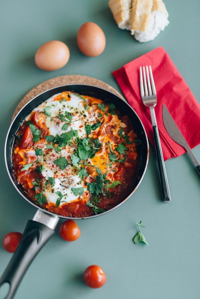 Tasty shakshuka with eggs, tomatoes, and herbs in a skillet, styled with bread and kitchenware.